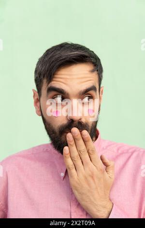Homme surpris couvrant la bouche avec la main contre le fond vert menthe Banque D'Images
