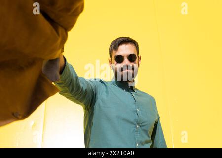 Homme souriant portant des lunettes de soleil et tenant une veste marron Banque D'Images
