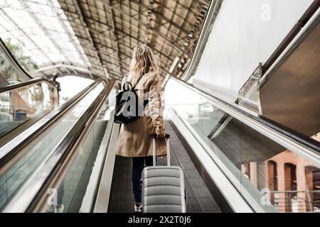 Femme tenant des bagages et se déplaçant dans l'escalier roulant à la gare Banque D'Images