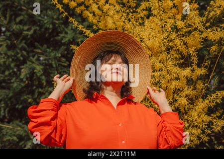 Femme mature portant un chapeau de paille et profitant de la lumière du soleil près de l'arbre de fleur jaune Banque D'Images