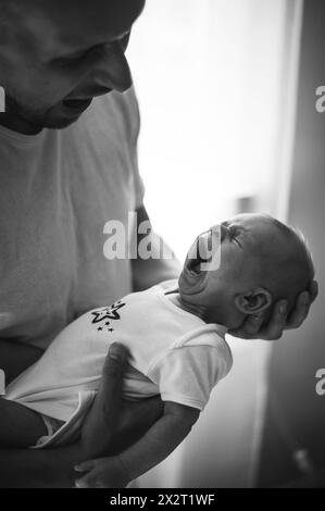 Bébé garçon pleurant dans les bras de son père à la maison Banque D'Images