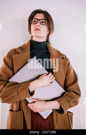 Jeune femme d'affaires debout avec ordinateur portable devant le mur au bureau Banque D'Images