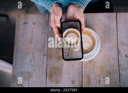 Femme prenant une photo de café par téléphone intelligent au café Banque D'Images