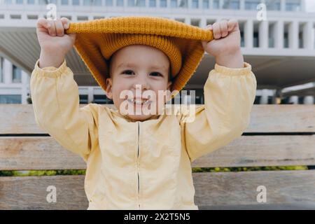 Garçon souriant tirant un chapeau tricoté orange Banque D'Images