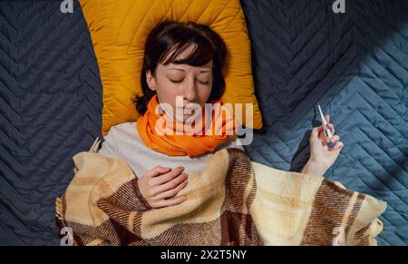 Femme malade avec thermomètre dormant sur le lit à la maison Banque D'Images