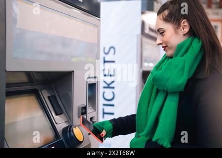 Femme souriante achetant billet par téléphone intelligent à la gare Banque D'Images