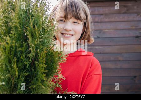 Fille souriante avec une frange brune derrière l'usine Thuja Banque D'Images