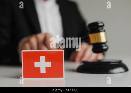 Main du juge tenant un marteau en bois. Drapeau de la Suisse. Concept de système judiciaire suisse Banque D'Images