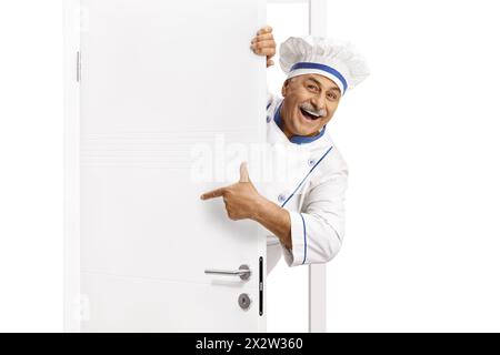 Chef mûr dans un uniforme poitning à une porte et souriant Banque D'Images