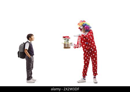 Écolier surpris regardant un clown effectuer un tour avec un chapeau et des fleurs isolé sur fond blanc Banque D'Images