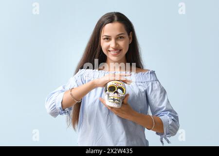 Jeune femme heureuse avec crâne humain peint sur fond bleu Banque D'Images