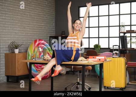 Heureuse employée de bureau assise sur la table dans le bureau. Concept de vacances d'été Banque D'Images