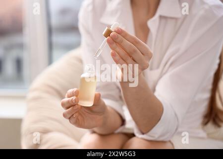 Jeune femme avec une bouteille d'huile de CBD à la maison, gros plan Banque D'Images