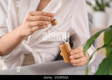 Jeune femme avec une bouteille d'huile de CBD à la maison, gros plan Banque D'Images