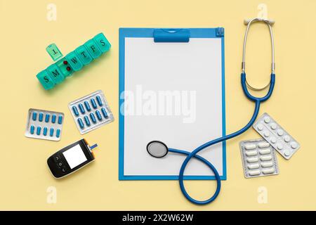 Presse-papiers vierge avec pilules, stéthoscope et glucomètre sur fond jaune. Journée mondiale de la santé Banque D'Images