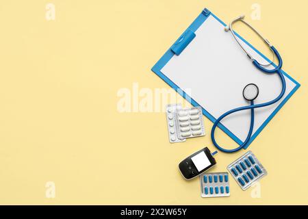 Presse-papiers vierge avec pilules, stéthoscope et glucomètre sur fond jaune. Journée mondiale de la santé Banque D'Images