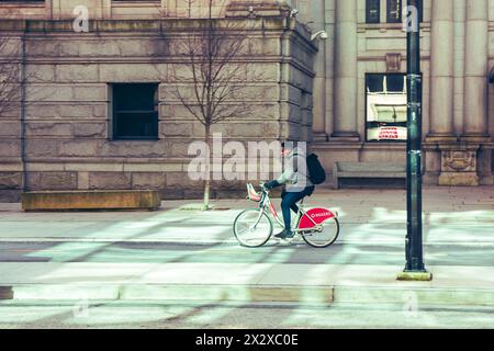 Un homme conduisant un vélo partagé dans la piste cyclable de la rue Hornby, devant le bâtiment de la Vancouver Art Gallery illuminé par la lumière réfléchie. Banque D'Images