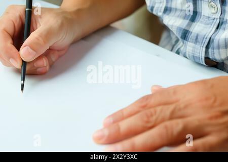 Homme avec chemise à carreaux commence à écrire tenant un stylo à bille sur une feuille de papier vierge. La main est prête pour l'écriture. Bloc d'écriture Banque D'Images