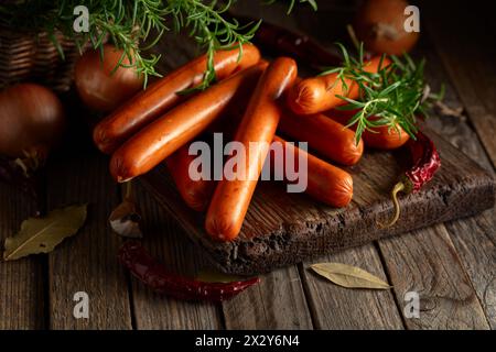 Saucisses savoureuses avec romarin, oignon, ail, poivron rouge et feuilles de laurier. Saucisses sur une table de cuisine. Banque D'Images