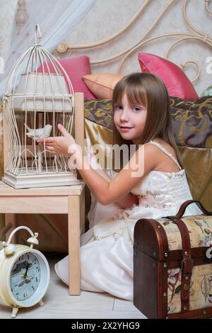 Petite fille dans la chambre à coucher jouant avec un oiseau dans une cage Banque D'Images