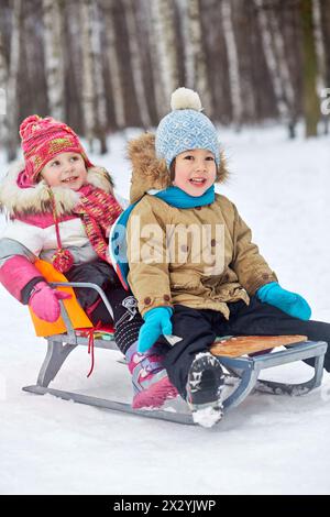 Deux petits enfants souriants assis dans la luge dans le parc d'hiver Banque D'Images