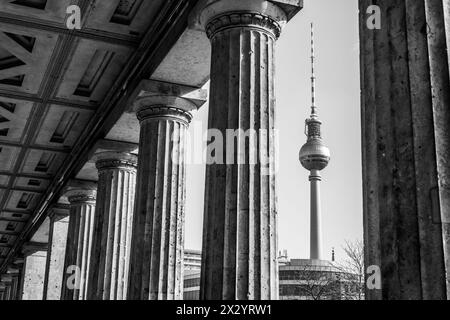 La tour de télévision de Berlin est haute, encadrée par les colonnes classiques d'un bâtiment historique voisin par temps clair. Berlin, Allemagne. Image en noir et blanc. Banque D'Images