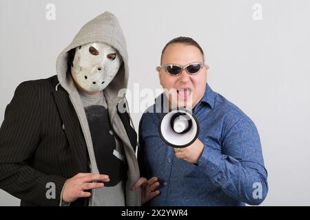 Deux hommes, l'un portant un masque, l'autre portant des lunettes de soleil avec mégaphone Banque D'Images