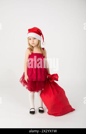 La fille dans une robe rouge avec un arc dans la cloche Père Noël avec sac cadeaux Banque D'Images