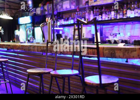 Tabourets de bar en métal inhabituels se tiennent près du comptoir de bar dans la lumière bleue. Banque D'Images