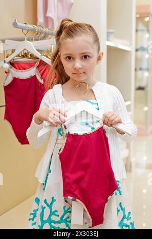 Petite fille tient un cintre avec maillot de bain fermé Banque D'Images