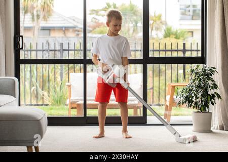 Un garçon aspire le salon avec un aspirateur sans fil moderne. Nettoyage, technologie sans fil Banque D'Images