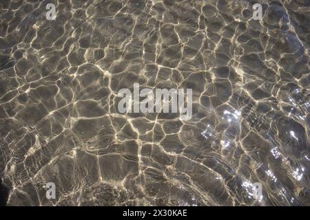 Eau de mer claire avec la lumière du soleil créant des motifs chatoyants sur le fond sablonneux Banque D'Images