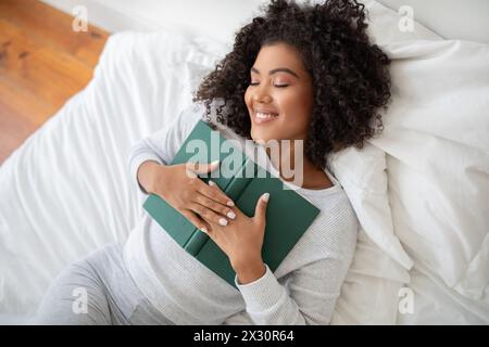 Femme couchée dans le lit tenant un livre Banque D'Images