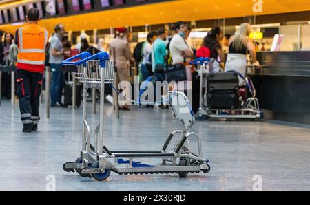 Ein Kofferwagen wurde am Flughafen Zürich stehen gelassen. Dahinter checken einige Personen für ihre Flug ein. (Zürich, Schweiz, 16.07.2022) Banque D'Images