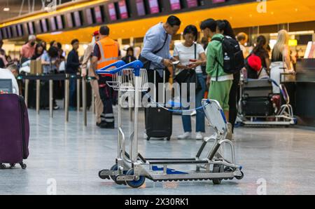 Ein Kofferwagen wurde am Flughafen Zürich stehen gelassen. Dahinter checken einige Personen für ihre Flug ein. (Zürich, Schweiz, 16.07.2022) Banque D'Images