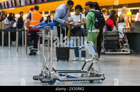 Ein Kofferwagen wurde am Flughafen Zürich stehen gelassen. Dahinter checken einige Personen für ihre Flug ein. (Zürich, Schweiz, 16.07.2022) Banque D'Images