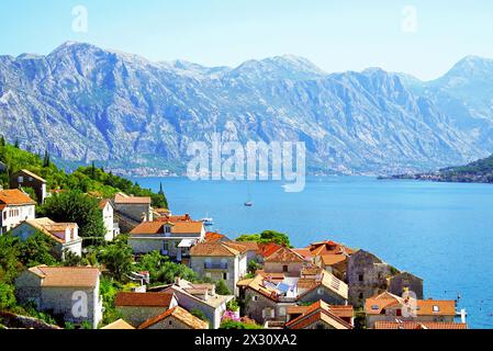 Toits de tuiles rouges de maisons dans la ville monténégrine de Perast sur fond de la mer lumineuse et des montagnes majestueuses Banque D'Images