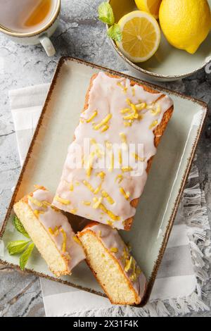 Lemon Drizzle Cake est un gâteau britannique classique connu pour sa texture humide et sa saveur vibrante de citron en gros plan sur l'assiette sur la table. Vie supérieure verticale Banque D'Images