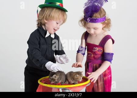 Deux enfants en costumes magiciens et deux chatons sur une table ronde Banque D'Images