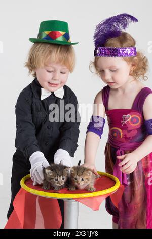 Deux enfants en costumes magiciens et deux chatons sur une table ronde Banque D'Images