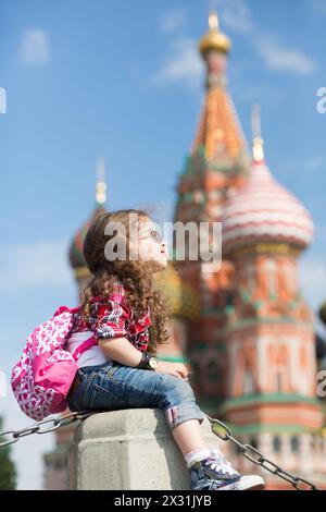 La petite fille mignonne en robe élégante et lunettes de soleil près de la cathédrale assis sur le béton Banque D'Images