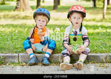 Fatigués petits scooteristes se reposent assis sur le trottoir de la passerelle dans le parc Banque D'Images