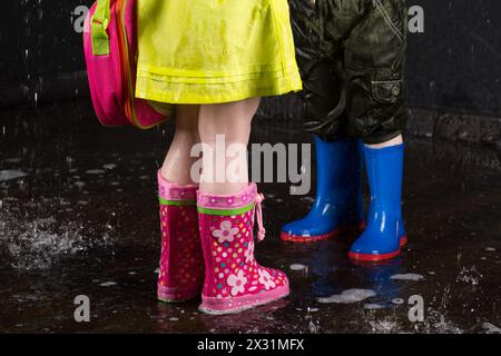 Jambes d'enfants portant des bottes en caoutchouc colorées dans l'eau Banque D'Images