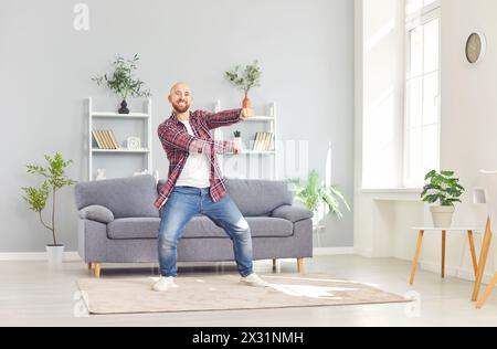 Jeune homme amusant heureux portant des vêtements décontractés dansant dans le salon à la maison. Banque D'Images