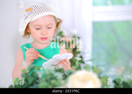 Petite fille en béret blanc avec des peintures à l'aquarelle dans les mains Banque D'Images