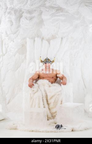 Un homme musclé dans le casque viking avec de la neige sur le corps assis dans la chaise de neige Banque D'Images