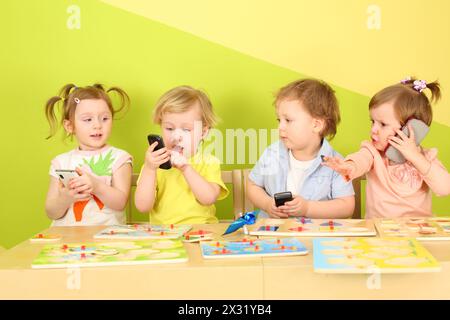 Deux garçons et deux filles avec des téléphones dans les mains sont assis à une table avec des jouets Banque D'Images