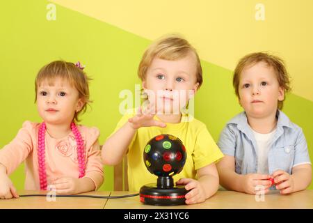 Deux garçons et une fille sont assis à la table, le garçon au centre tenant le ballon avec des lumières Banque D'Images