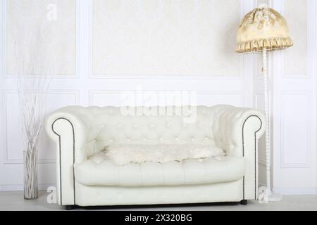 Canapé en cuir blanc dans la chambre avec lampadaire et papiers peints blancs. Banque D'Images