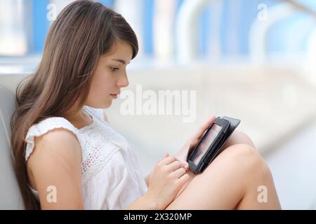 Jolie fille dans la blouse blanche regarde la tablette pc sur le sol dans la galerie longue lumière. Banque D'Images